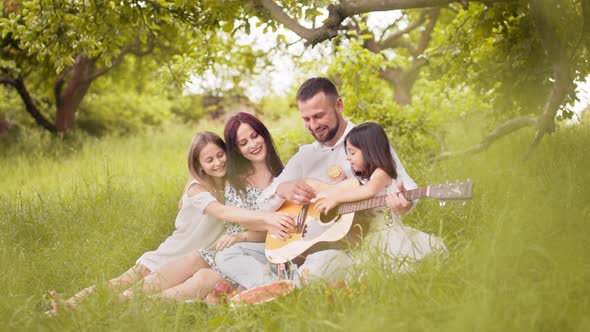 Happy Family with Cute Daughters Having Picnic at Green Garden with Guitar Songs