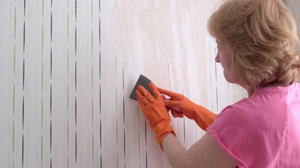 An Adult Woman Takes Off the Wallpaper Works with a Spatula in the Room