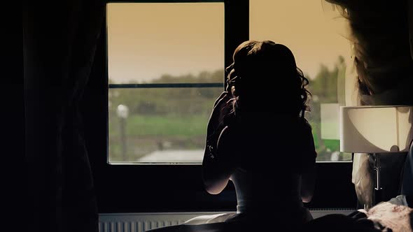 Young Beautiful Girl Sits in Front of a Window Bride Silhouette