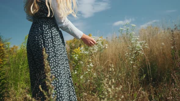 A Young Girl in a Beautiful Dress Sniffs Wildflowers