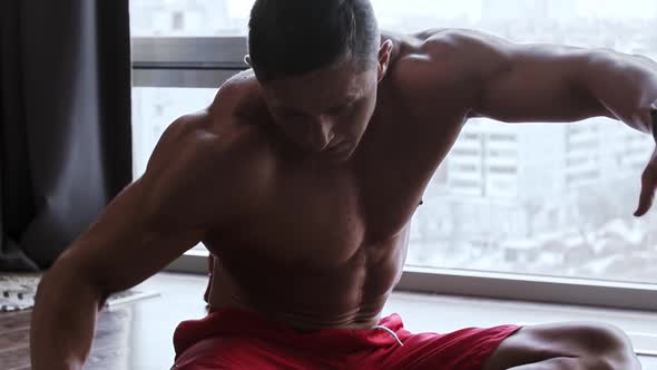 Muscular Man Sitting on the Floor and Stretching His Hands and Body to His Legs