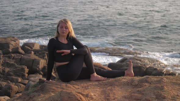 Pretty Girl in Black Tracksuit Sits on Grey Rocky Cliff