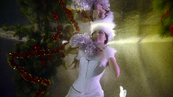 Winter Sorceress Woman Is Playing Silver Tinsel Underwater in Pool with Christmas Tree