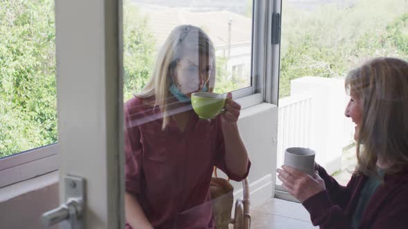 Mother and daughter talking to each other while drinking coffee at home
