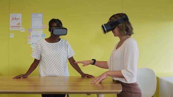 Two diverse female coworkers standing at desk, testing vr googles