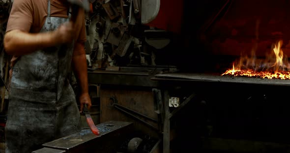 Blacksmith hammering a hot metal rod 