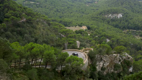 Cars driving on a curvy road i the mountains, partly covered by trees. No camera movements. Filmed i