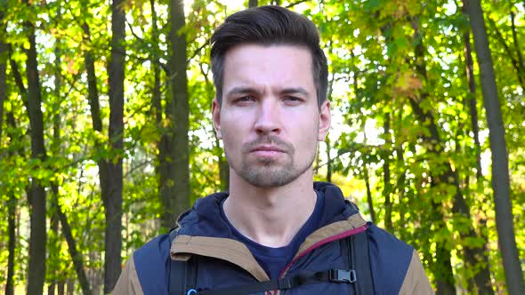 A Young Handsome Hiker Looks Seriously at the Camera in a Forest on a Sunny Day, Face Closeup