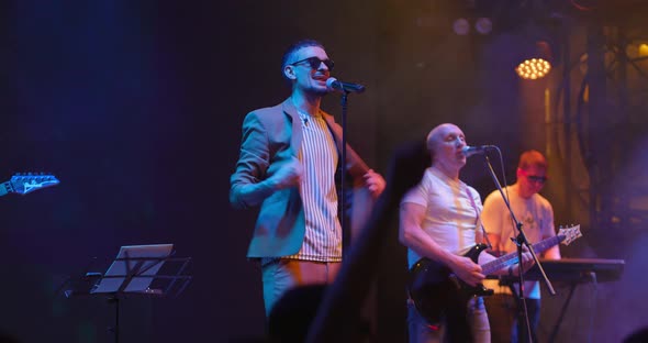 Attractive Young Male Singer in Glasses Performing with Band at Live Music Event
