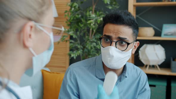 Arab Man in Face Mask Talking To Doctor at Home Checking Temperature Coughing