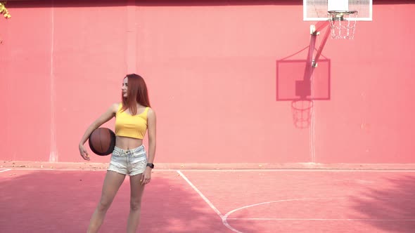 Beautiful Young Athletic Woman with a Ball on a Street Basketball Court