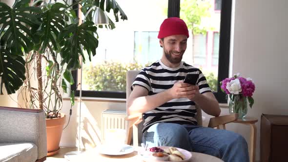 Attractive young man with a phone in his hands sitting in a cozy cafe.