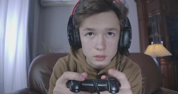 Close-up Portrait of Brunette Brown-eyed Teenager in Headphones Using Game Console. Focused Boy