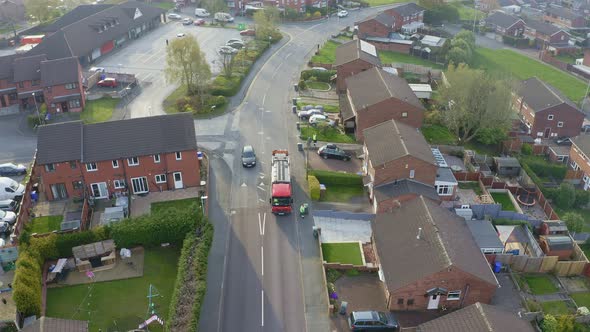 A bin lorry, refuse collection vehicle makes it way up the road as men load recycling bins into the