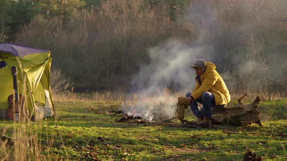 A Young Man Chops Wood Near the Fire in the Forest