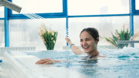 Attractive Young Woman Having Hydrotherapy in Luxury Pool Touching Water Stream with Hand and