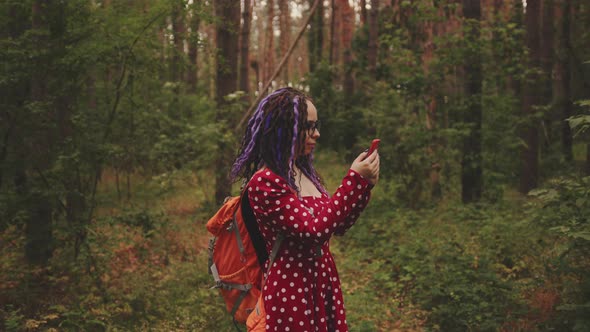 Traveling woman with dreadlocks with a phone in woods.