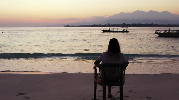 Silhouette of woman sitting on exotic beach, watching romantic sunset with beautiful colorful light