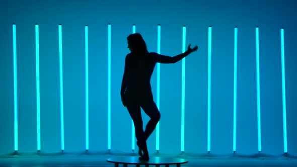 A Slim Athletic Woman Gracefully Moves Against the Backdrop of Bright Multicolored Neon Tubes