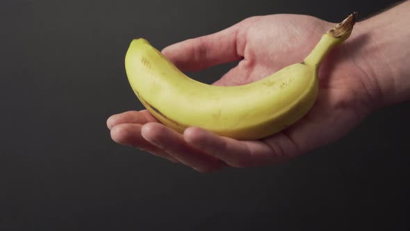 Ripe juicy unpeeled banana sways in the hand of a young man 