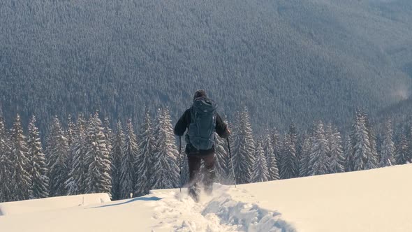 Successful Hiker with Backpack Walking on Snowy Mountain Hillside on Cold Winter Day