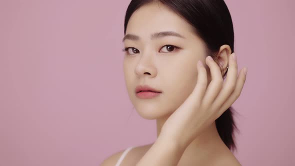 Close up face of beautiful young Asian woman with clear skin lifting eye on pink background.