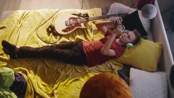 Teen Guitarist Using Smartphone on Bed