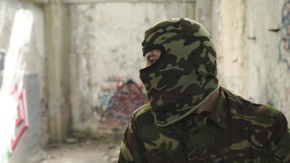 Soldier in Camouflage Uniform Looks Around and at Camera in Ruins