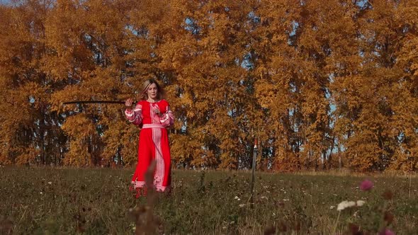 Militant Concept on an Autumn Field - Feisty Blonde Woman in Red Dress Training Her Swordplay