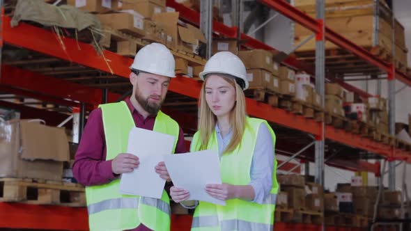 Man Woman in Overalls Check Documents Against Background Large Boxes Goods