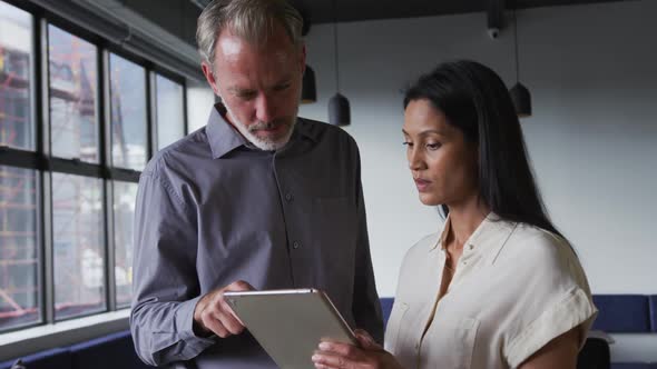 Diverse business colleagues standing using digital tablet and talking in office