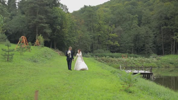 Groom with Bride Walking Near Lake in the Park. Wedding Couple. Slow Motion