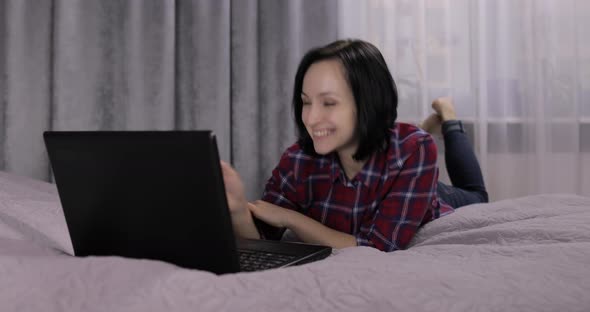Young Woman Lying on Bed and Having Video Chat Using Webcam on Laptop Computer