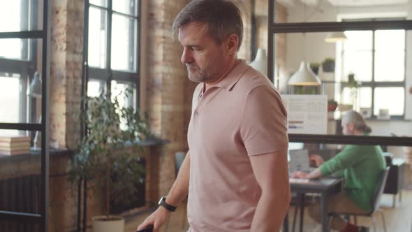 Mature Businessman Walking to Office Desk and Using Laptop