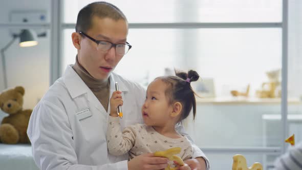 Asian Pediatrician Sitting with Little Girl and Talking to Her Mom