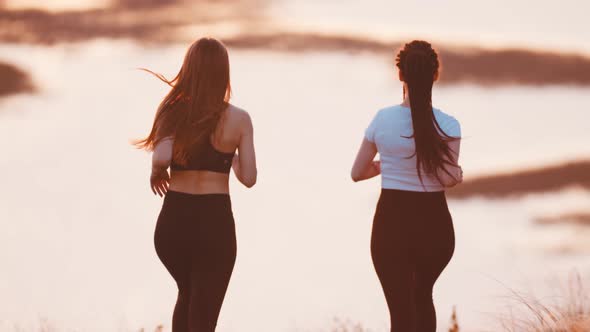 Two Young Women Jogging on Wheat Field While Sunset