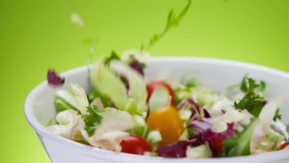 Fresh salad falling into bowl on green background