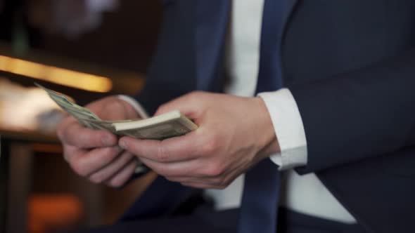 Closeup Businessman Counts US Dollars While Sitting on a Chair in a Clothing Store