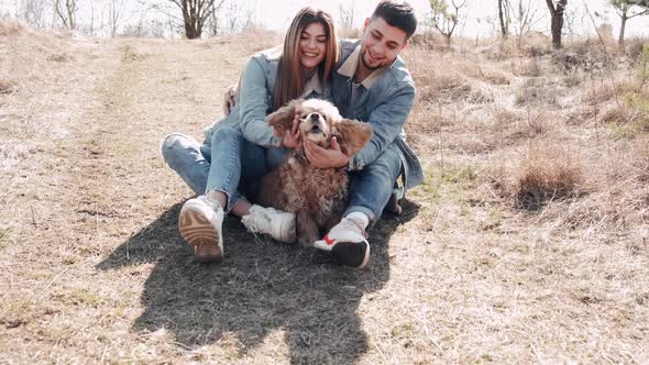 Pretty Young Woman and Man Are Sitting in the Field Walking with a Cute Dog