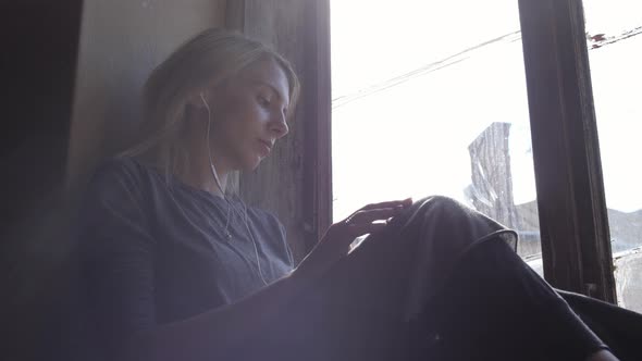 Girl sitting on a window sill and listening 