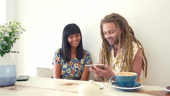 Black hair asian girl discuss with caucasian dreadlock man sitting at the table in coffee shop and w