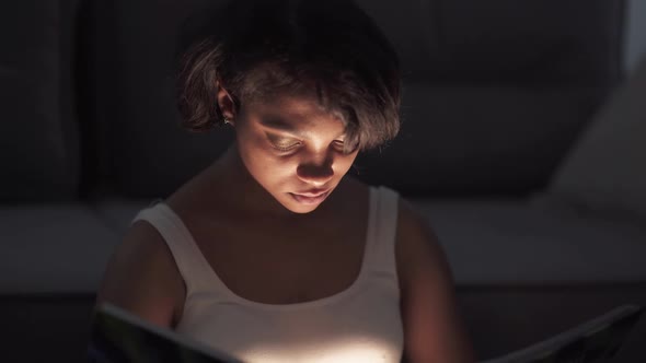 Portrait of Young Female Sitting at Home on the Floor and Reading a Book Warm Light Selfisolation