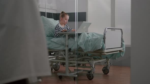 Sick Child Relaxing in Bed Playing Cartoon Video Games on Laptop Computer During Medical Examination