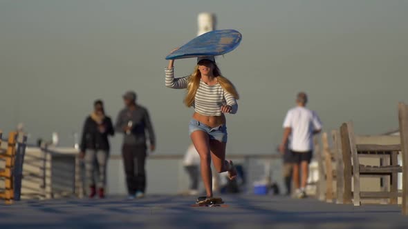 A young woman longboard skateboarding while balancing a surfboard on her head.