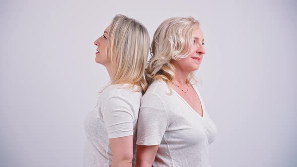 Two Blonedhaired Focused Peaceful Women in Their 40s Standing Back to Back Looking Dreamy Wearing