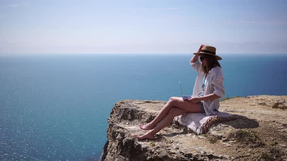 Successful Business Woman in Yellow Hat Working on Laptop By the Sea