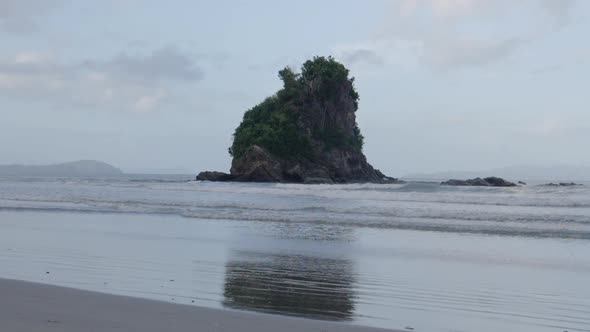 Small waves breaking and swashing on beach with limestone island in the horizon in ultra slow motion