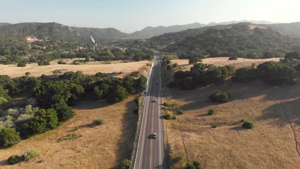 Cars Drive on Highway Through Green Canyon and Fields Followed by Drone