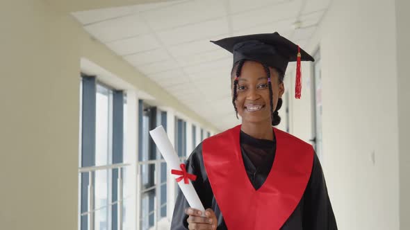 African American Female Graduate in Mantle Stands with a Diploma in Her Hands and Smiles