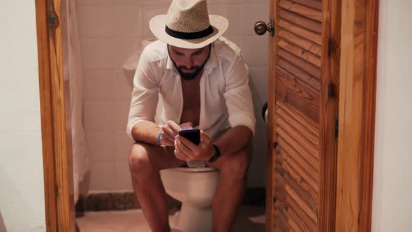 Calm Happy Healthy Young Guy In Hat Resting And Sitting On Toilets Cabin In Vacation Resort. WC